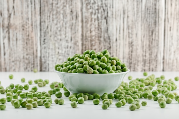 Free photo peas in a white bowl on white and grungy wooden wall. side view.