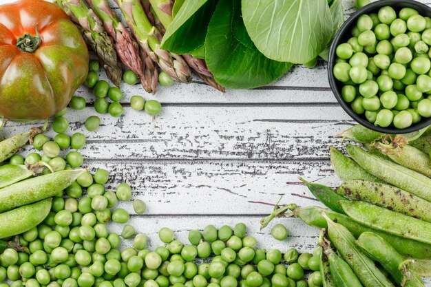 Peas with tomato, bok choy, green pods, asparagus in a bucket on wooden wall, flat lay.