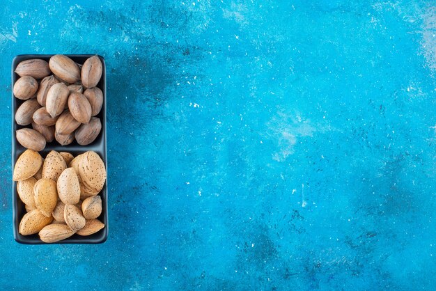 Pecan and almonds in a bowl on the blue surface