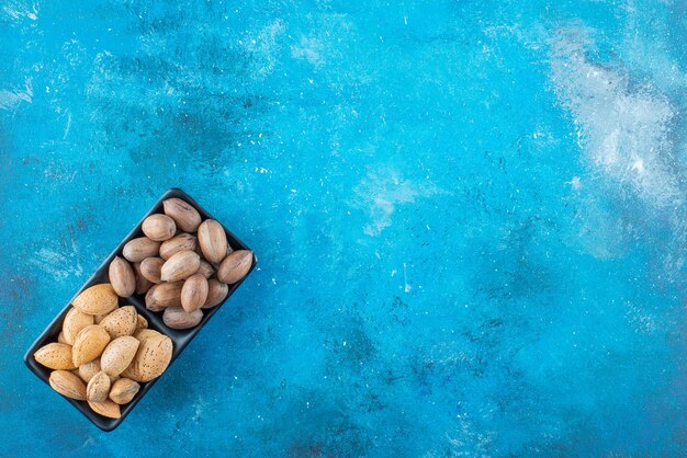 Pecan and almonds in a bowl , on the blue table. 