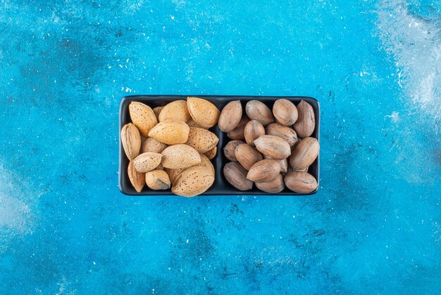 Pecan and almonds in a bowl , on the blue table. 