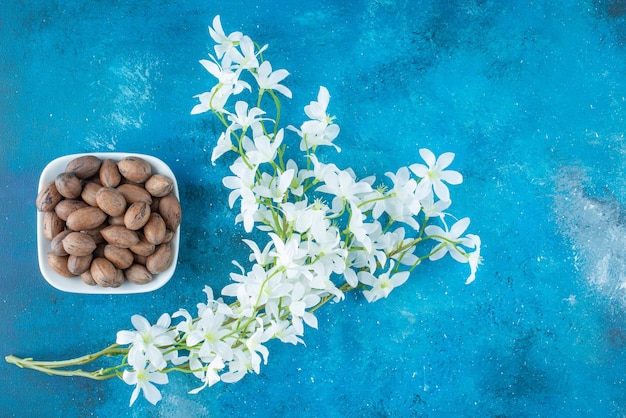 Foto gratuita noci pecan in una ciotola accanto ai fiori, sul tavolo blu.
