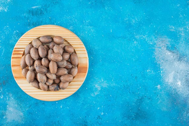 Pecan nuts on a wooden plate on the blue surface