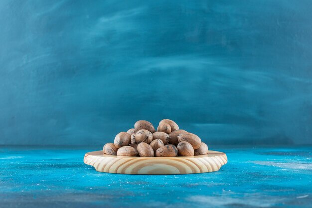 Pecan nuts on a wooden plate on the blue surface