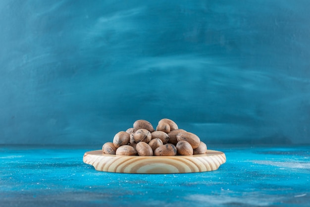 青いテーブルの上の木の板のピーカンナッツ。