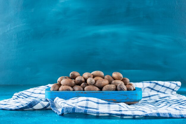 Орехи пекан в деревянной тарелке на кухонном полотенце, на синем столе.