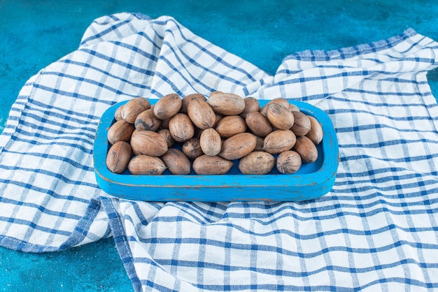 Free photo pecan nuts in a wooden plate on a tea towel , on the blue table.