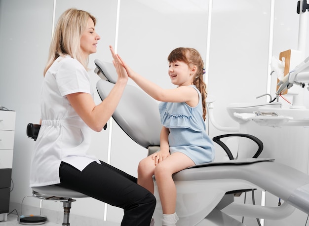 Pediatric dentist and adorable little girl giving high five