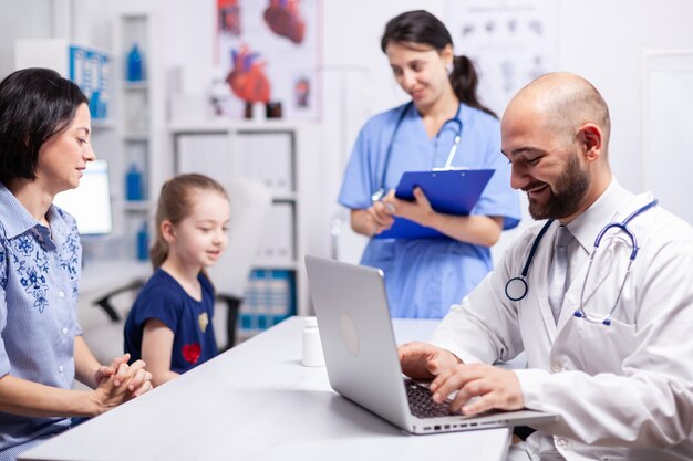 Pediatrician doctor and nurse sitting at desk in medical office talking with child. Healthcare practitioner specialist in medicine providing professional radiographic treatment in hospital clinic