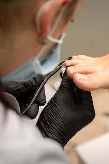 Мастер педикюра использует кусачки для ногтей во время обрезки ногтей на ногах в педикюрном салоне.