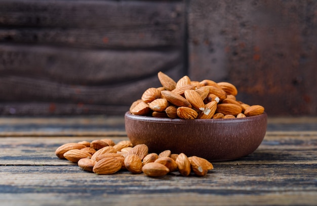 Peeled almonds in a clay plate on stone tile and wooden background