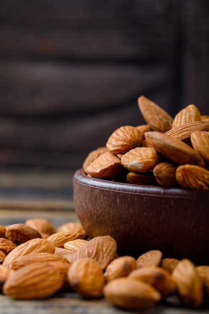 Peeled almonds in a clay plate on stone tile and wooden background.