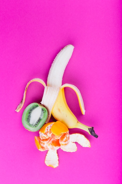 Free photo peeled banana; orange and halved kiwi on pink background