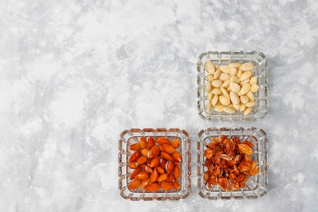 Peeled (blanched) and unblanched whole almonds in glass bowls on grey concrete 