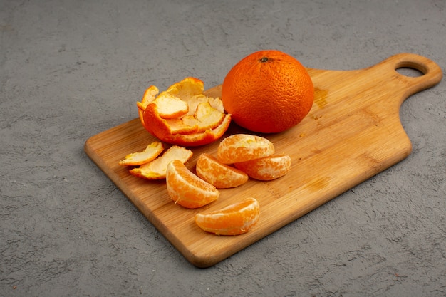 Peeled out tangerines along with whole and sliced fruit on a brown desk