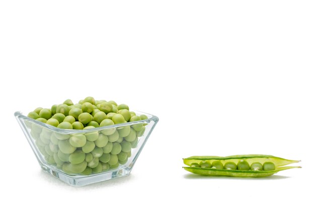 Peeled peas in a glass container with some peas in the shell on one side on a white background