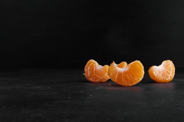 Peeled and sliced mandarin orange on black background, profile view. 