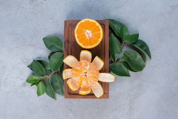 Peeled and sliced tangerines on a small board on marble background. 