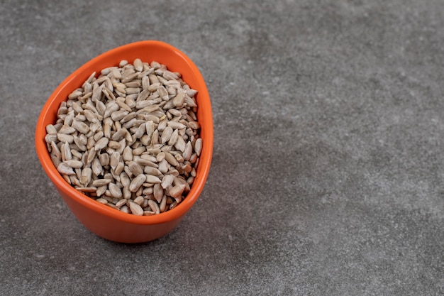 Peeled sunflower seeds in orange bowl over grey surface. 