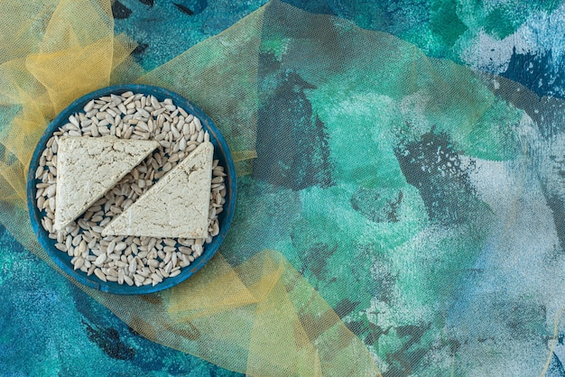 Peeled sunflower seeds and sliced halva on the wooden plate on tulle , on the blue table.