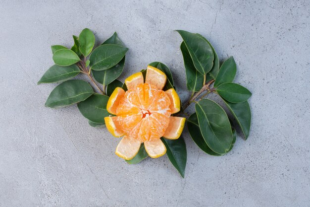 Peeled tangerine and decorative leaves on marble background. 