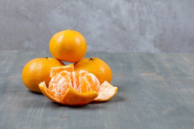 Peeled tangerine with whole tangerines on marble surface