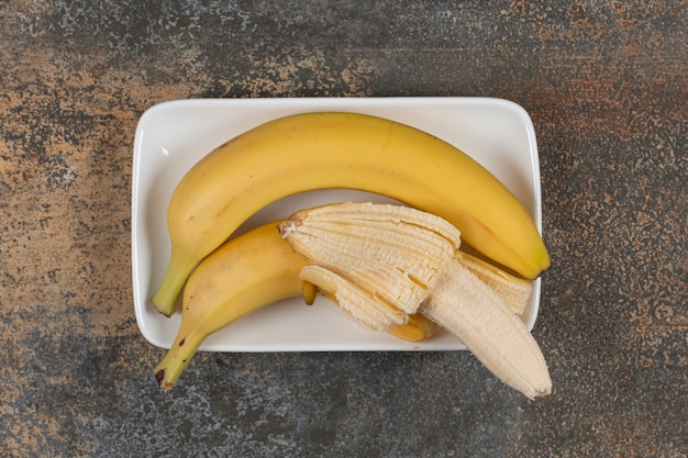 Peeled and unpeeled bananas on white plate
