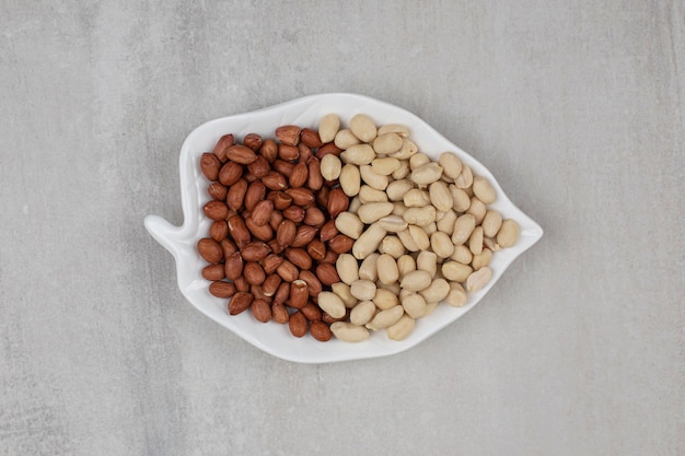 Peeled and unpeeled peanuts on leaf shaped plate.