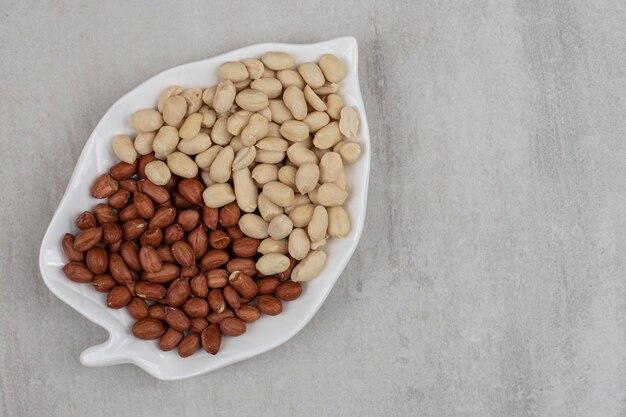 Peeled and unpeeled peanuts on leaf shaped plate.