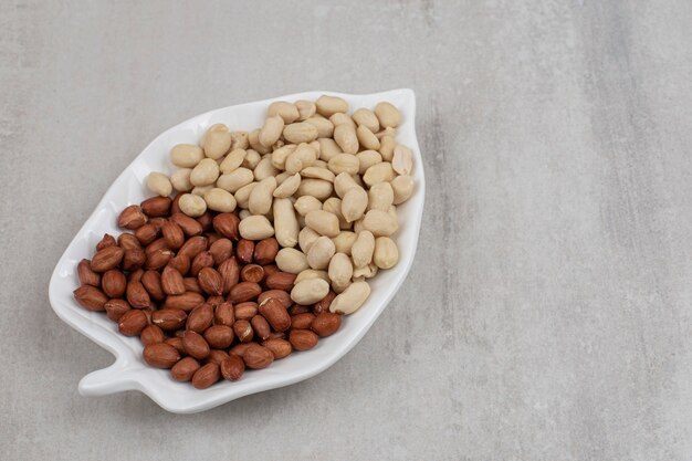 Peeled and unpeeled peanuts on leaf shaped plate.