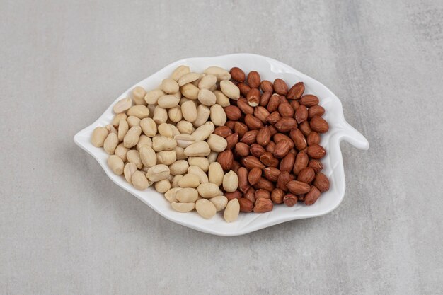 Peeled and unpeeled peanuts on leaf shaped plate.