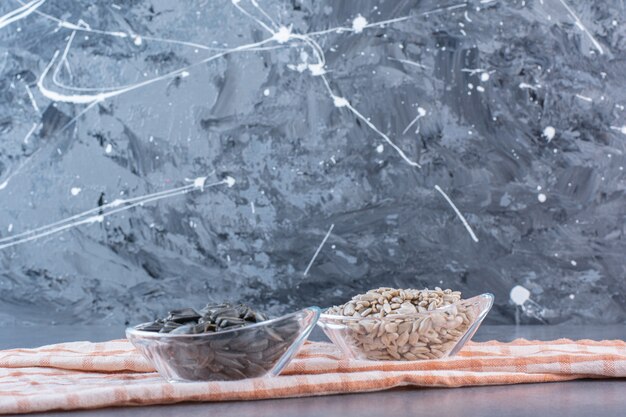 Peeled and unpeeled sunflower seeds in bowls on tea towel , on the marble surface