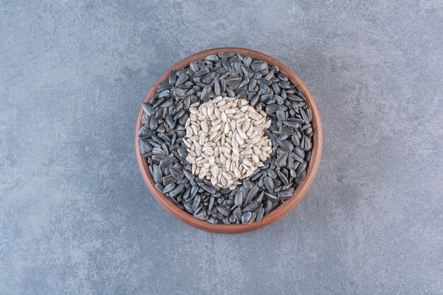 Peeled and unpeeled sunflower seeds in wooden bowl, on the marble surface