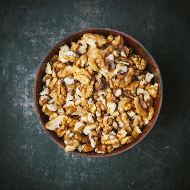 Peeled walnuts in a brown bowl on dark table