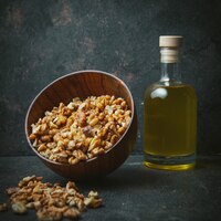 Бесплатное фото Очищенные грецкие орехи в коричневой миске с маслом грецкого ореха в стеклянной бутылке сбоку на темном столе