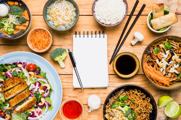 Pen on blank spiral notepad surrounded with thai traditional food on wooden table