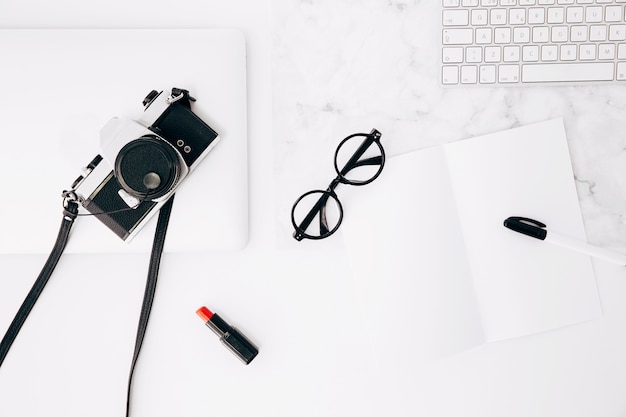 Pen and eyeglasses on paper; red lipstick; camera; keyboard and digital tablet on desk