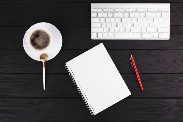 Pen near notepad, cup on saucer, spoon and keyboard