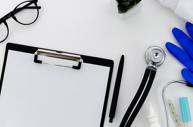 Pen; paper on clipboard; eyeglasses; gloves and medical equipment on white backdrop