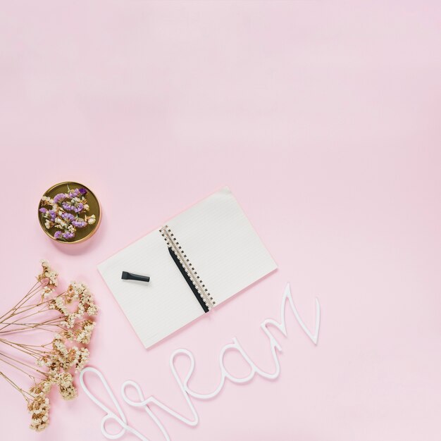 Pen on spiral notebook with flowers and dream text on pink background