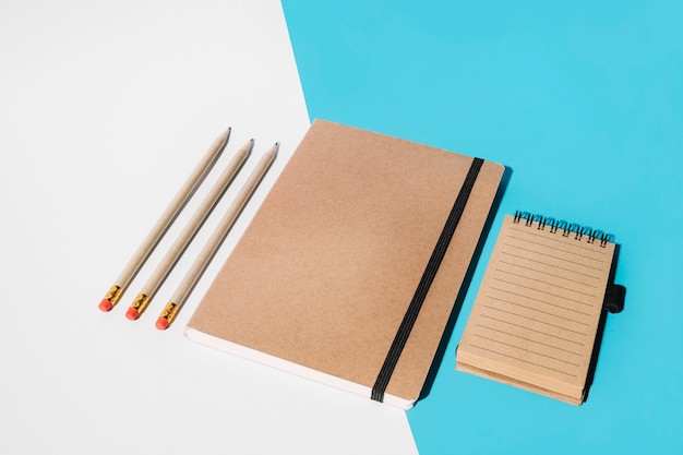 Pencil; closed notebook and spiral notepad on white and blue backdrop