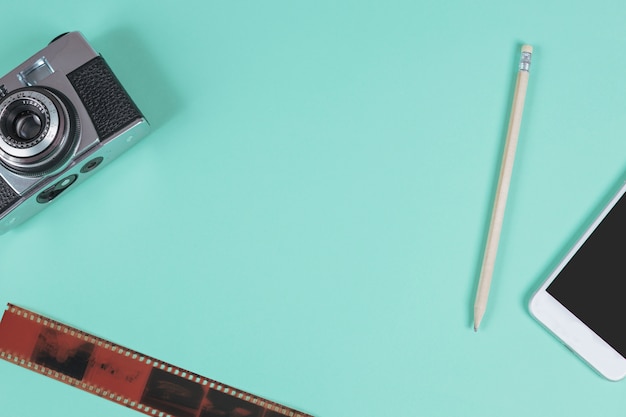 Pencil; mobile phone; camera and an old film strip against turquoise background