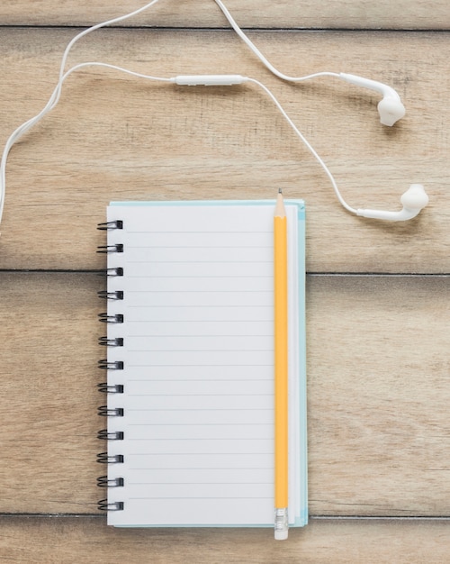 Pencil on opened notebook near earphones on wooden table