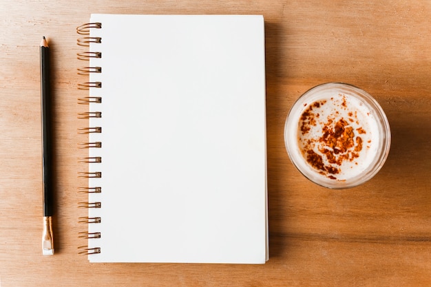 Pencil; spiral blank notepad and coffee on wooden backdrop