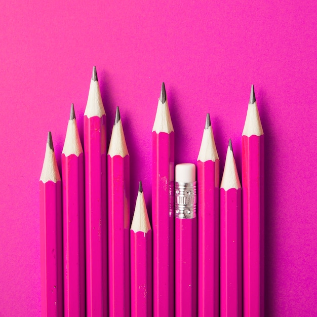 Free photo pencil with eraser standing out from other sharp pencils on pink backdrop