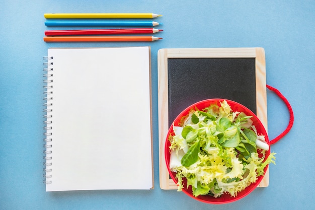 Foto gratuita matite e insalata vicino a notebook e lavagna