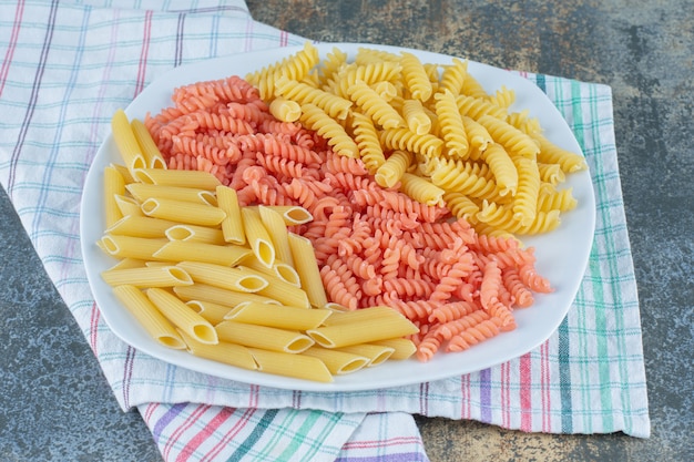 Foto gratuita penne e fusilli in ciotola su asciugamano, sullo sfondo di marmo.