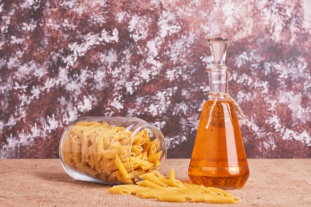 Penne pasta in a jar with a bottle of oil. 