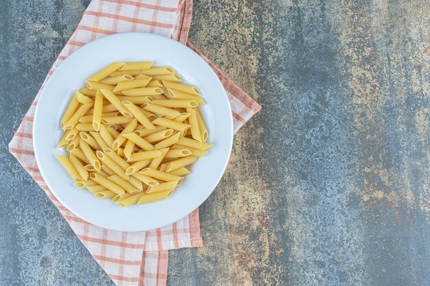 Penne pasta on the plate, on the towel , on the marble surface.