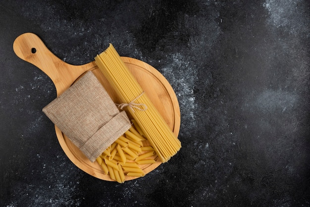 Penne pasta in a rustic basket with spaghetties on a wooden platter.